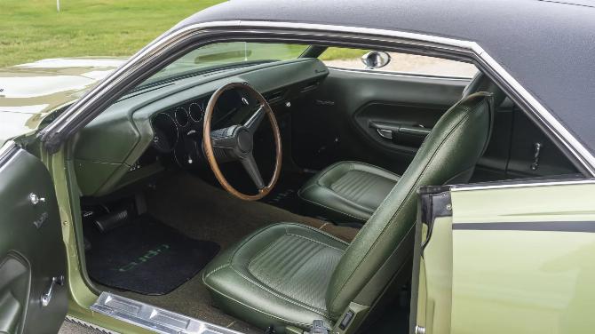 Передние сиденья автомобиля Plymouth Barracuda 1970 года выпуска цвета лайм-зелен с черным виниловым верхом и зеленой виниловой обивкой, вид через открытую дверь водителя.